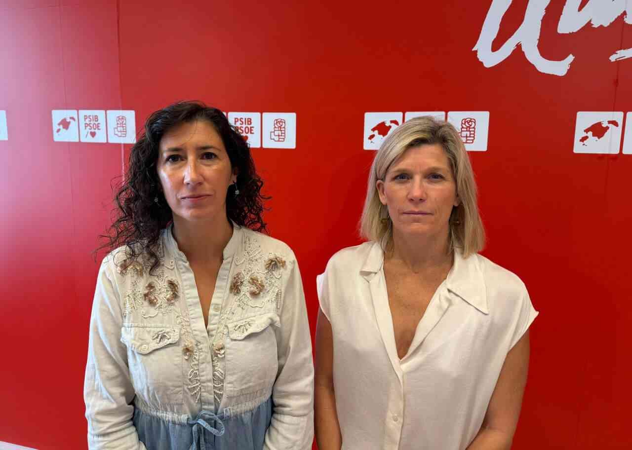 Amanda Fernández y Sofía Alonso de pie posando ante una pared roja con logotipos del PSIB-PSOE
