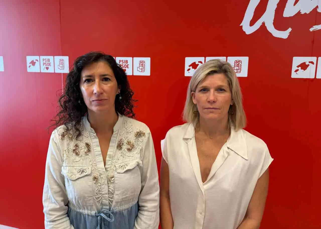 Amanda Fernández y Sofía Alonso de pie posando ante una pared roja con logotipos del PSIB-PSOE