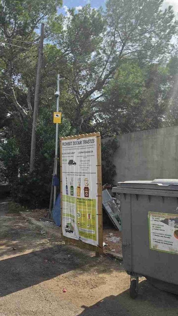 Cartel de madera que prohíbe tirar trastos junto a contenedores y cámara de seguridad