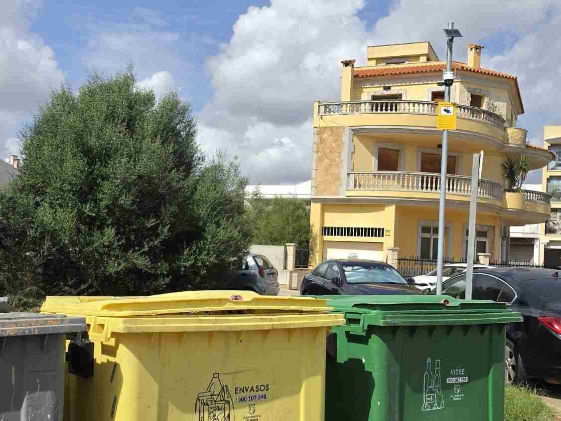 Contenedores de basura y poste con cámara de vigilancia en una calle de Porto Cristo