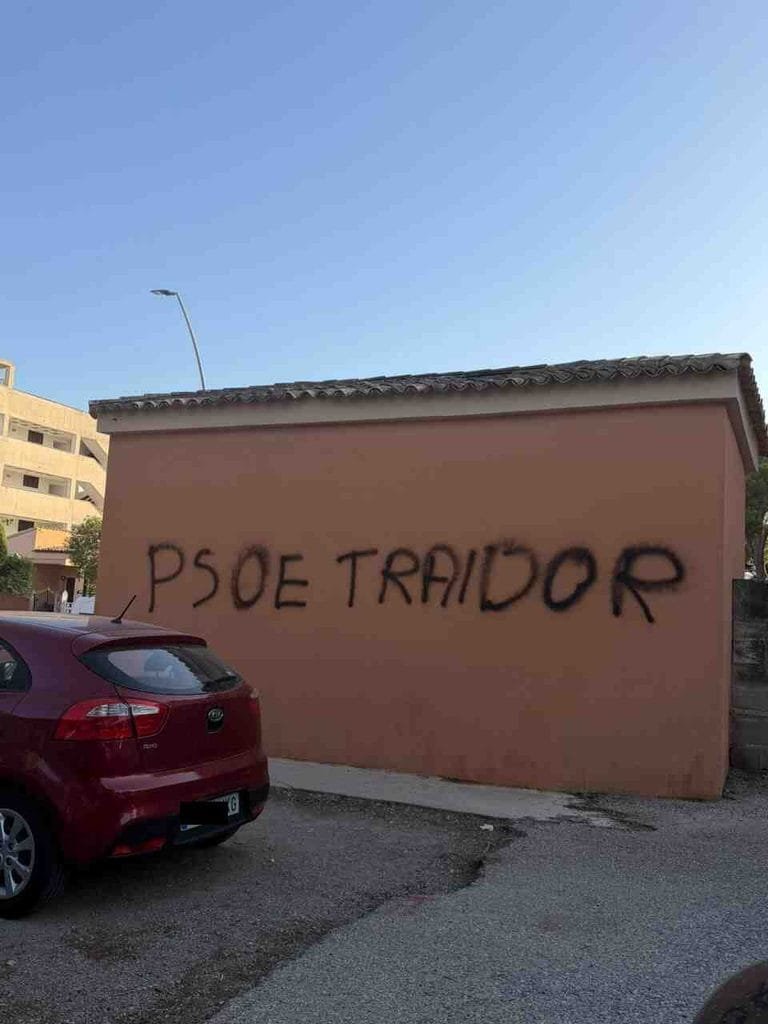 Detalle del grafiti en spray negro PSOE traidor sobre pared ocre en Cala Millor