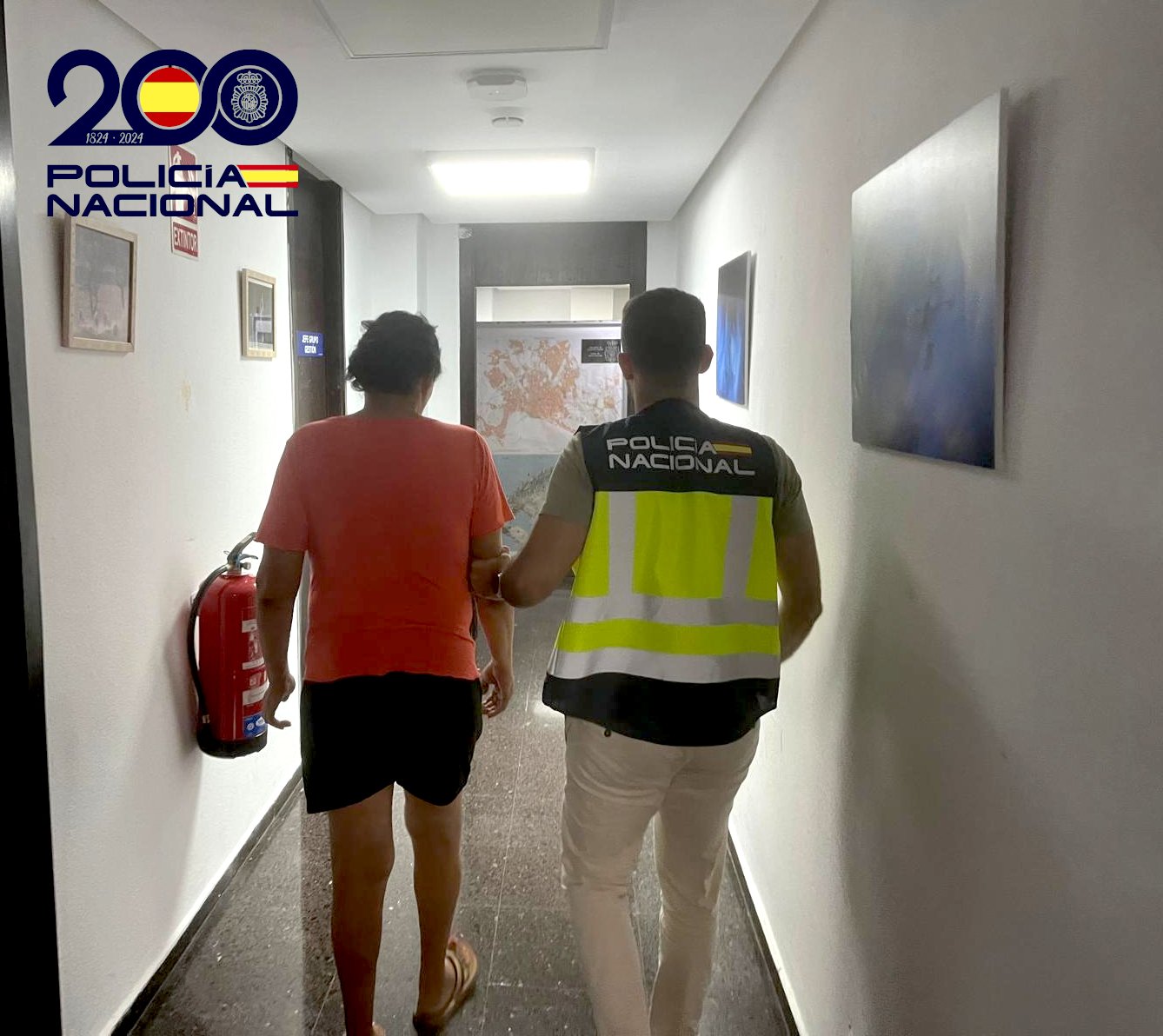 Agente de la Policía Nacional custodiando a una mujer detenida por un pasillo policial