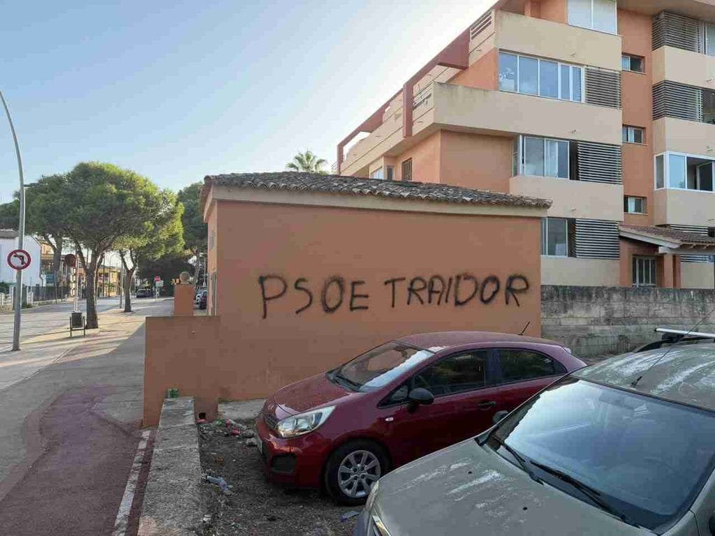 Detalle del grafiti en spray negro PSOE traidor sobre pared ocre en Cala Millor