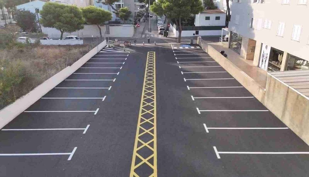 Aparcamiento recién asfaltado con franja central en aspa amarilla y plazas de estacionamiento pintadas en blanco