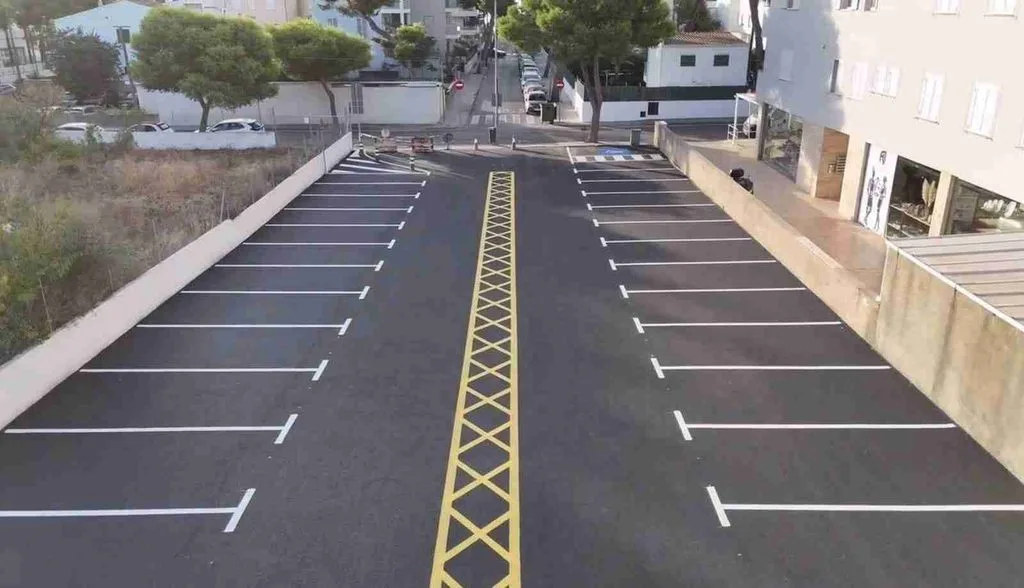 Aparcamiento recién asfaltado con franja central en aspa amarilla y plazas de estacionamiento pintadas en blanco