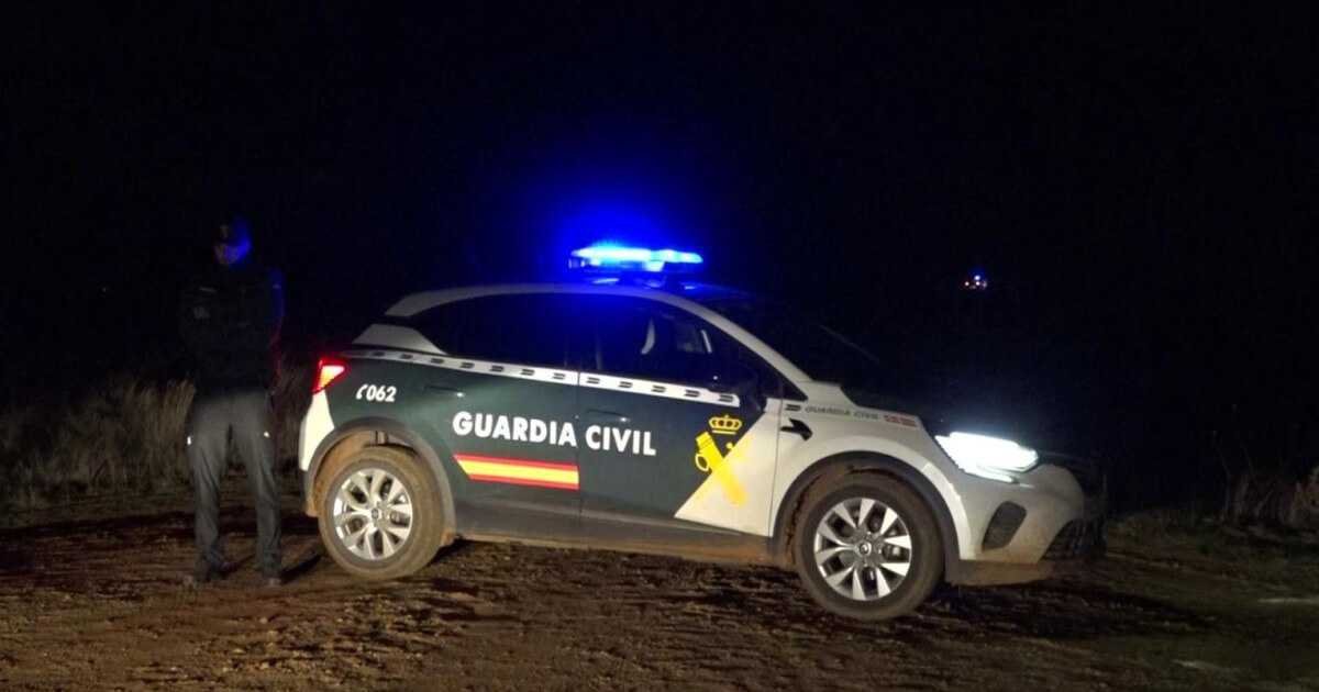 Coche patrulla de la Guardia Civil con luces azules encendidas y un agente de pie en un camino