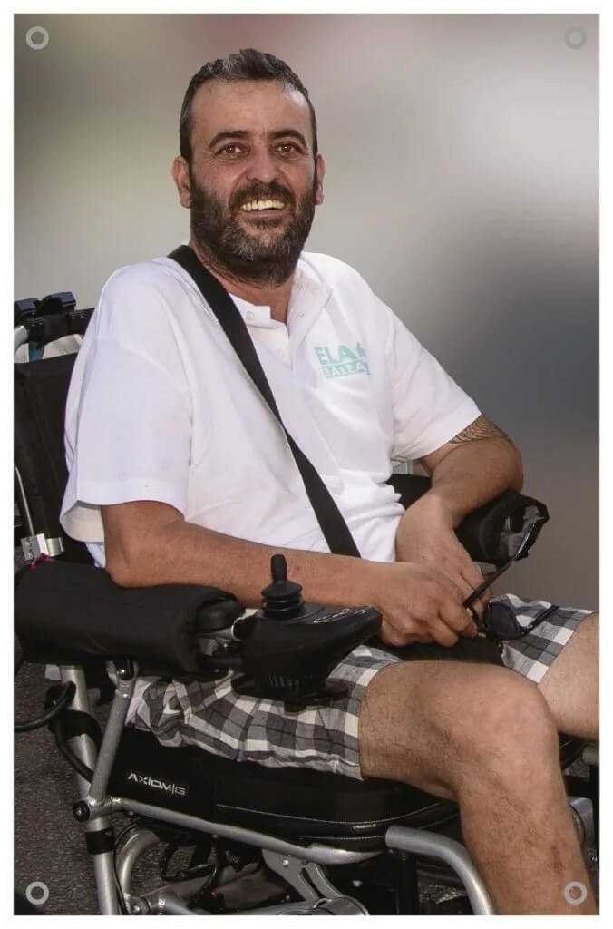 Santy Bassa sonriendo en su silla de ruedas con el polo oficial de ELA Balears