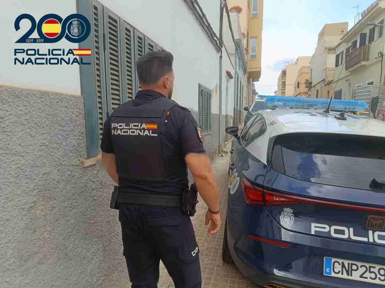 Agente de la Policía Nacional de espaldas junto a un vehículo patrulla en una calle de Manacor