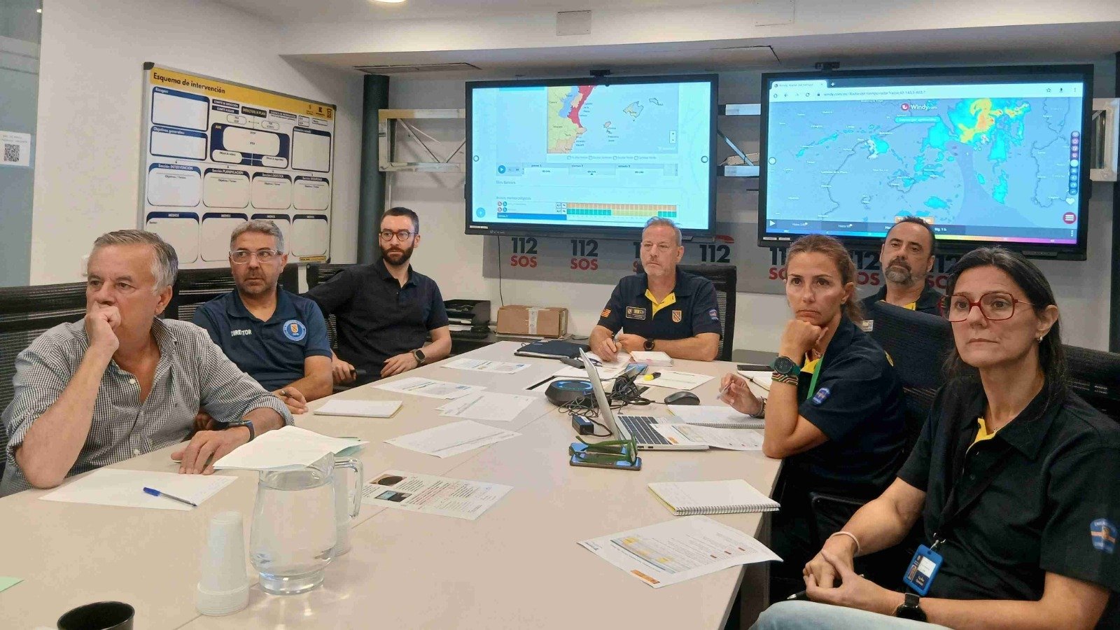 Miembros de Emergencias reunidos frente a pantallas con mapas meteorológicos analizando el temporal en Baleares